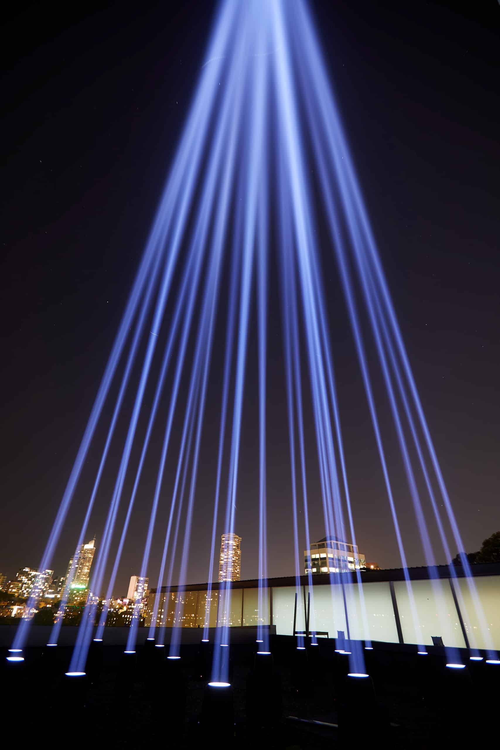 Beams of light are shooting down from the night sky against a background of well lit buildings.